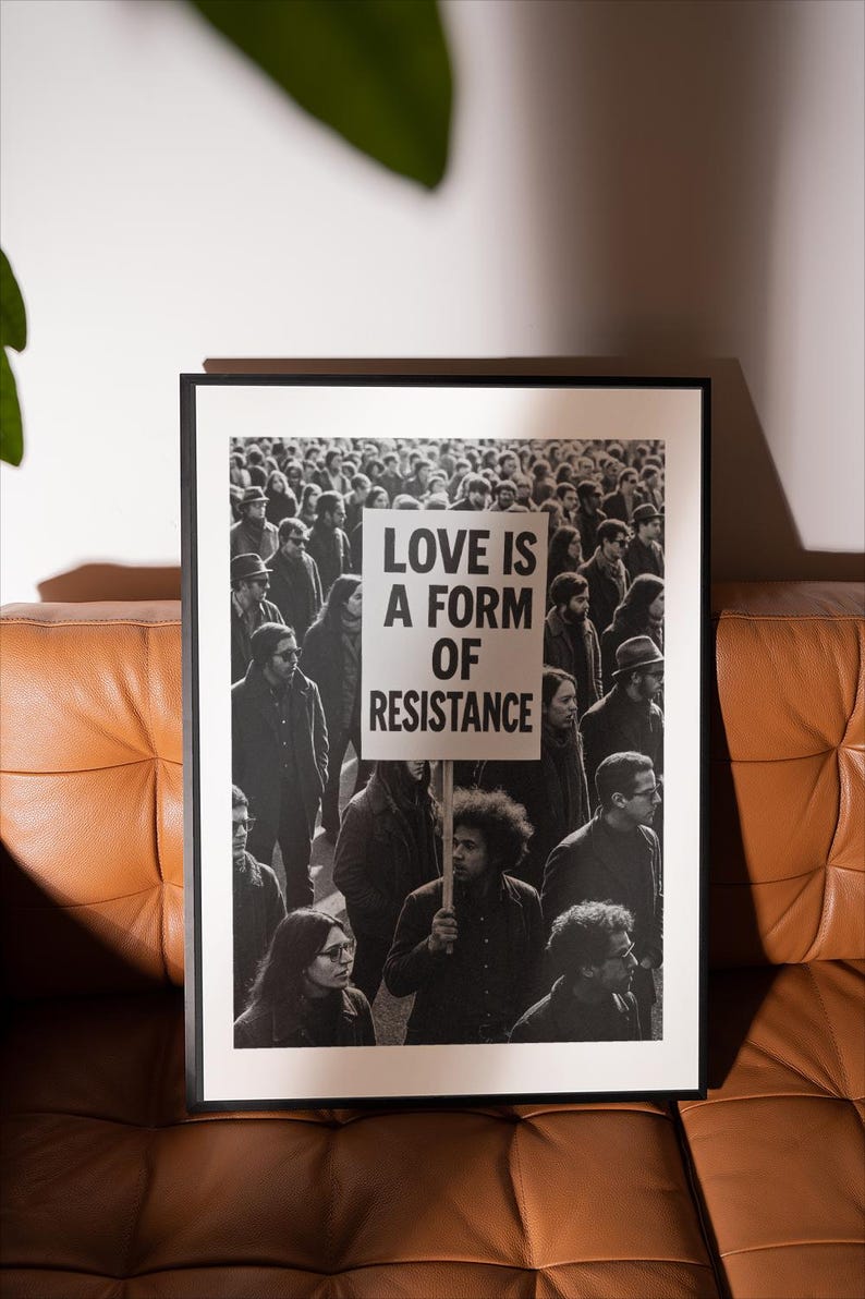 Pu&ograve; includere: Stampa in bianco e nero incorniciata raffigurante una folla. Un cartello con la scritta "LOVE IS A FORM OF RESISTANCE" &egrave; tenuto da una persona. La stampa &egrave; esposta su un divano in pelle marrone.