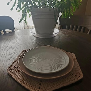 May include: A beige crocheted placemat with a white ceramic plate on top. The plate has a swirl design.