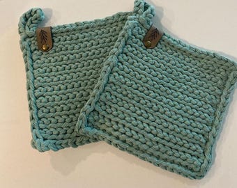 May include: Two teal blue knitted pot holders with leather tabs and a leaf design. The pot holders are made of a thick, textured yarn.