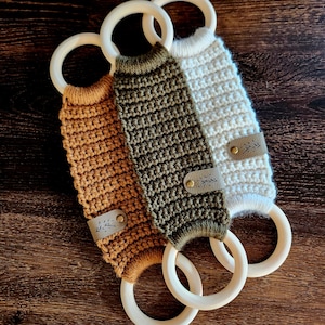 May include: Three crocheted teethers with wooden rings. The teethers are in brown, green, and white with leather tags.