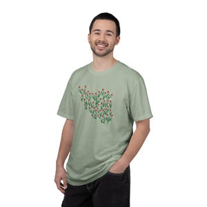 May include: A light green t-shirt featuring a floral design of red tulips with green stems and leaves. The short-sleeved shirt is made of a soft material and is worn by a person.