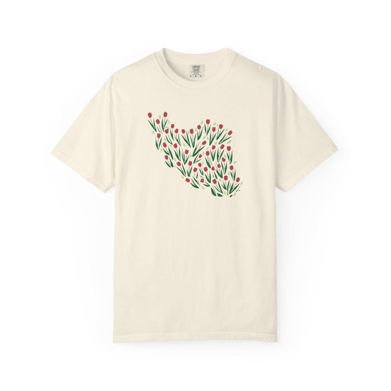 May include: Cream-colored t-shirt featuring a floral design in the shape of a country. The design is composed of red flowers with green stems and leaves. The shirt has short sleeves and a crew neck.