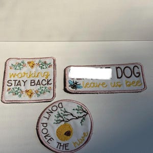 May include: Three embroidered patches with white fabric bases and pink borders. One square patch reads working STAY BACK with floral and honeycomb motifs. One rectangular patch reads DOG leave us bee with a bee. One circular patch reads DON'T POKE THE hive.