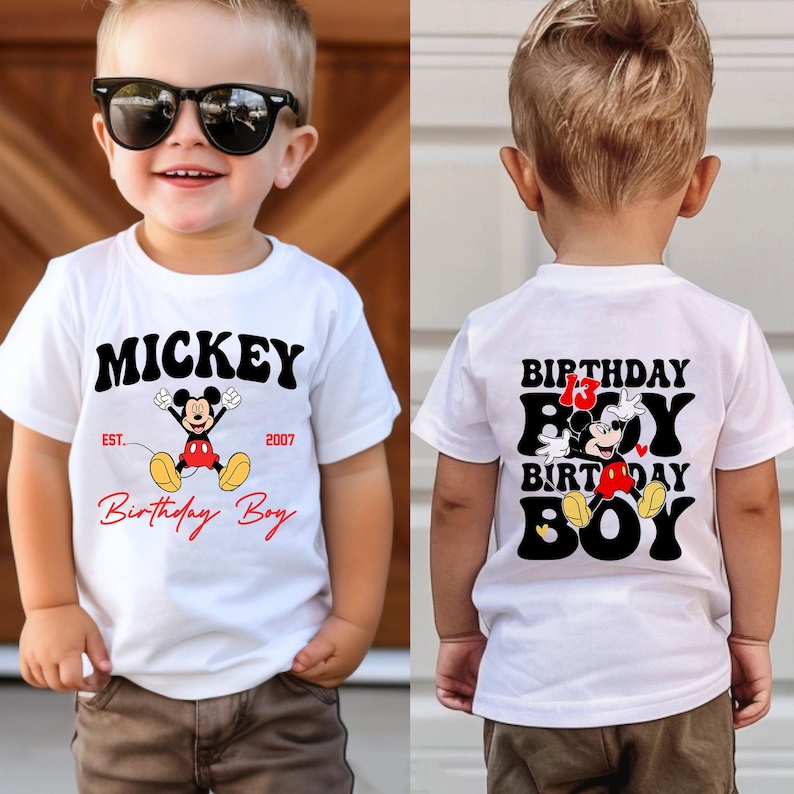 Op de afbeelding: Wit T-shirt met Mickey Mouse-ontwerp. De voorkant toont "Mickey", "Birthday Boy" en "Est. 2007" in zwart en rood. De achterkant van het shirt zegt "Birthday Boy" met een Mickey Mouse-afbeelding.
