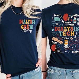Puede incluir: Camiseta azul marino con "DIALYSIS CREW" en texto colorido en la parte delantera y "Ashley" en cursiva. La parte trasera presenta ilustraciones médicas y las palabras "DIALYSIS TECH" con términos y símbolos médicos.