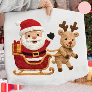Peut inclure: Un coussin blanc sur le thème de Noël avec un Père Noël crocheté en costume rouge et traîneau, avec un renne tirant le traîneau. Le Père Noël fait signe et le renne a des bois bruns. Un coffret cadeau doré est dans le traîneau.