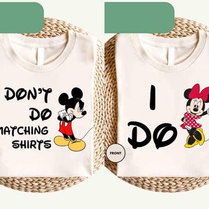 May include: Two cream-colored t-shirts with black text and cartoon characters. One shirt says "I DON'T DO MATCHING SHIRTS" with Mickey Mouse. The other says "I DO" with Minnie Mouse. Both shirts have "FRONT" printed on them.