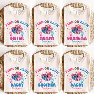 Puede incluir: Camisetas de color crema con el texto "PINK OR BLUE" sobre una imagen de dibujos animados de dos extraterrestres y huellas. Las camisetas tienen diferentes textos debajo, incluyendo "SISTER loves you", "MOMMY loves you", "GRANDMA loves you", "DADDY loves you" y "BROTHER loves you".