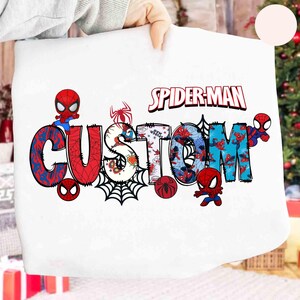 May include: White fabric featuring the words "SPIDER-MAN CUSTOM" in a colorful, comic-style design. The word "CUSTOM" is in large, stylized letters with Spider-Man imagery and a spider web. The "SPIDER-MAN" text is in red and white.