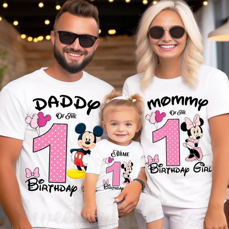 May include: White t-shirts with black text and pink accents. The shirts feature the words "Daddy", "Mommy", and "Birthday Girl" with the number "1" and Mickey and Minnie Mouse designs. A family is wearing the shirts.