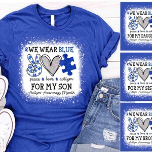 May include: Royal blue t-shirt with a white distressed design. The shirt features a peace sign, heart, and puzzle piece with the text "WE WEAR BLUE" and "FOR MY SON" for Autism Awareness Month. White sneakers are visible.