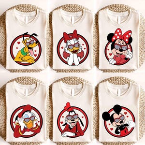 May include: Six off-white t-shirts featuring Disney characters Pluto, Daisy Duck, Minnie Mouse, Donald Duck, Goofy, and Mickey Mouse. Each character is wearing heart-shaped sunglasses and is inside a red circle with a white background.