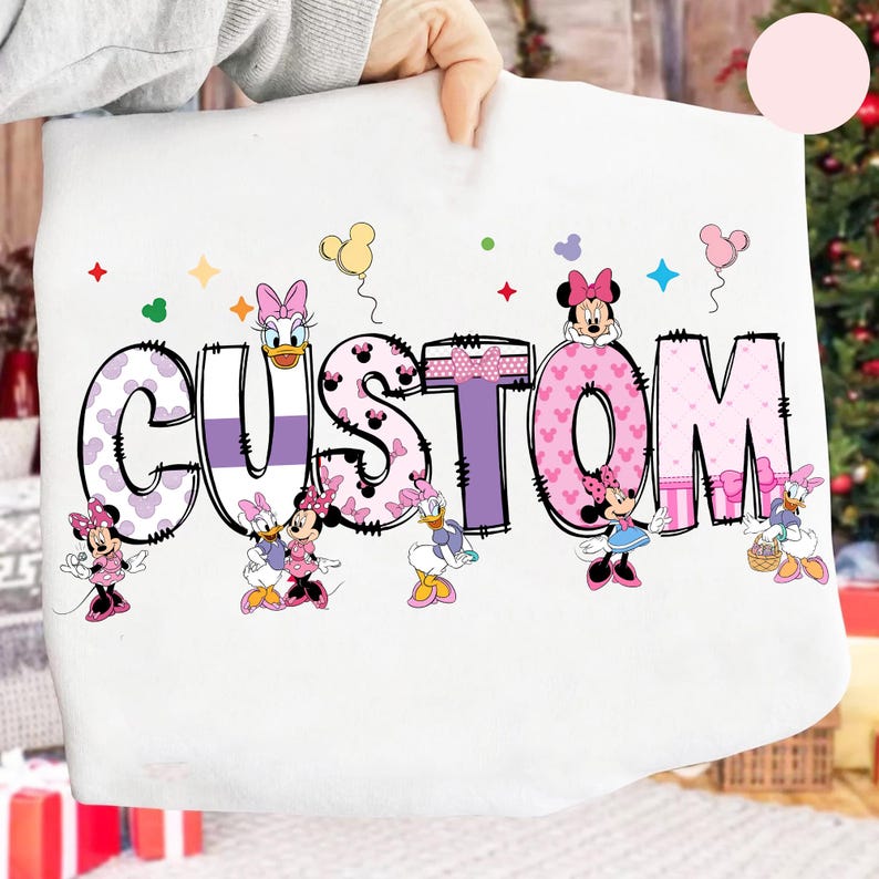 Op de afbeelding: Een witte deken met het woord "CUSTOM" in een groot, kleurrijk ontwerp. De letters zijn gevuld met stippen en patronen, met stripfiguren als Minnie Mouse en Daisy Duck. Kleurrijke sterren en ballonnen versieren de achtergrond.