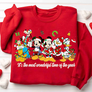 May include: Red sweatshirt featuring Disney characters Mickey Mouse, Minnie Mouse, Donald Duck, Daisy Duck, Goofy, and Pluto, all dressed in Christmas attire and wrapped in string lights. The text "It's the most wonderful time of the year" is printed on the front.