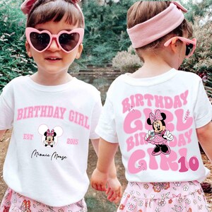 May include: Two children wearing white t-shirts with pink text that says "BIRTHDAY GIRL" and a Minnie Mouse graphic. The front of the shirt has "EST 2015" and "Minnie Mouse" text. The back of the shirt has "GIRL 10". They wear pink sunglasses and headbands.
