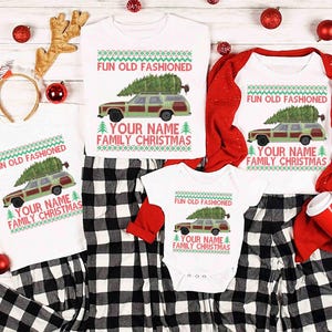 May include: A set of white Christmas-themed tops and a baby bodysuit. Each item displays a green and brown station wagon with a Christmas tree, and the text "FUN OLD FASHIONED YOUR NAME FAMILY CHRISTMAS". The tops are styled with black and white checked pyjama bottoms.