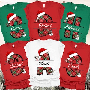 May include: A collection of Christmas-themed t-shirts in red, green, and white. Each shirt features a large letter design in a red and green plaid pattern, topped with a Santa hat. Names are printed across the letters. Snowman and reindeer graphics are also included.