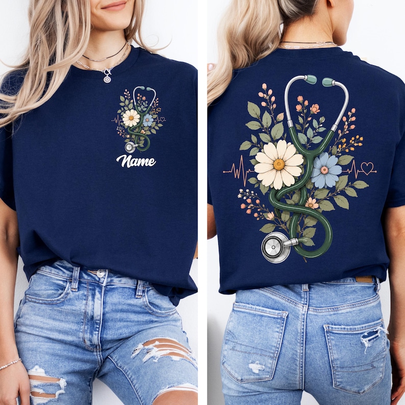 May include: Navy blue t-shirt featuring a floral design with a stethoscope and the word "Name". The design includes daisies, blue flowers, and green leaves. The back of the shirt has a similar design with a heartbeat line.