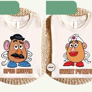 Può includere: Due magliette color crema con personaggi a forma di testa di patata dei cartoni animati. Una maglietta presenta una testa di patata maschile con baffi, cappello e la scritta "SPUD MUFFIN". L'altra maglietta ha una testa di patata femminile con un fiore, orecchini e la scritta "SWEET POTATO".