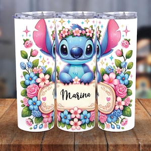 Puede incluir: Tres vasos aislados blancos con un personaje de dibujos animados azul con una corona de flores. Los vasos están decorados con flores rosas y azules, y el nombre "Marina" está escrito en una pancarta.