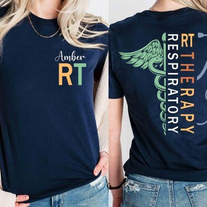 Puede incluir: Camiseta azul marino con "Amber RT" en blanco, naranja y verde en la parte delantera. La parte trasera presenta "RT RESPIRATORY THERAPY" en texto vertical con un caduceo y un gráfico de estetoscopio. Una camiseta de temática médica.