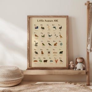 May include: A beige poster with a brown wooden frame titled "Little Aussie ABC". The poster features an alphabet chart with Australian animals and their corresponding letters. Each letter is paired with a colorful illustration of an animal, such as a koala, kookaburra, and echidna.