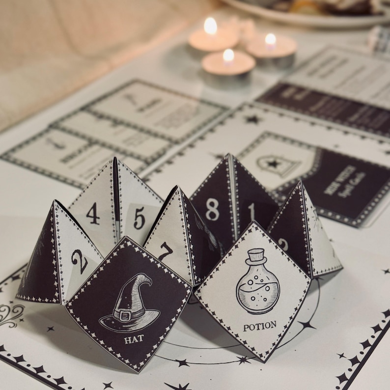May include: A black and white paper fortune teller with numbers 1 through 8 and images of a hat, potion, and a star. The fortune teller is folded and sitting on a white surface with a black and white star pattern.
