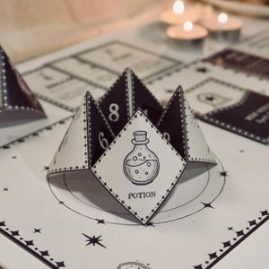 May include: A black and white printable potion-themed fortune teller game. The fortune teller is folded into a pyramid shape with the word "POTION" printed on the front. The fortune teller has numbers 6 and 8 printed on the sides.