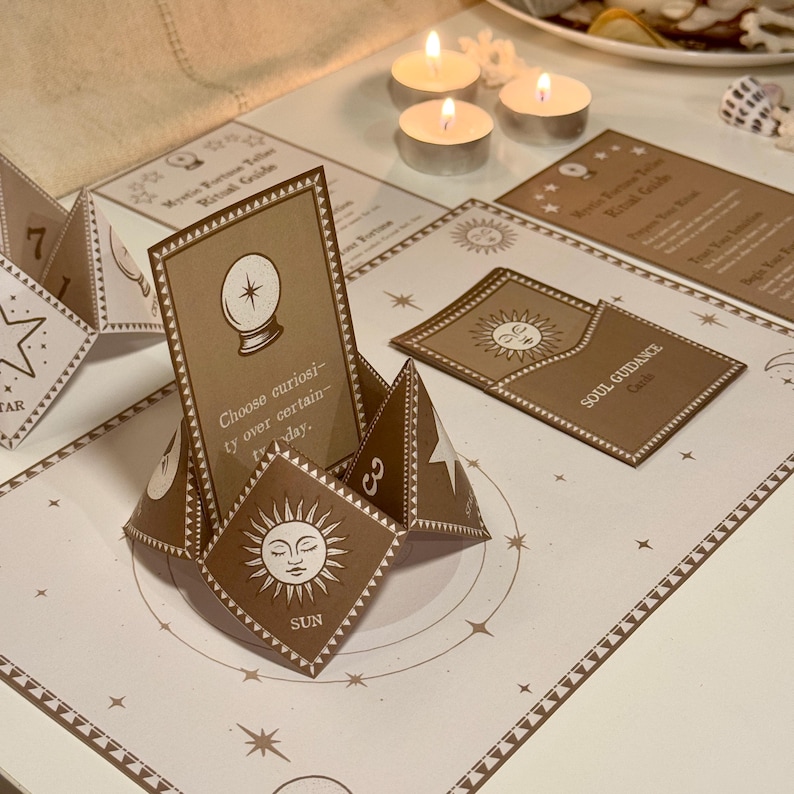 Op de afbeelding: Een bruin en wit fortuin vertelspel met een glazen bol, zon en sterren. Het spel is opgezet op een wit oppervlak met bruine accenten. De tekst op de kaarten luidt "Mystic Fortune Teller Ritual Guide" en "Kies nieuwsgierigheid boven zekerheid vandaag."