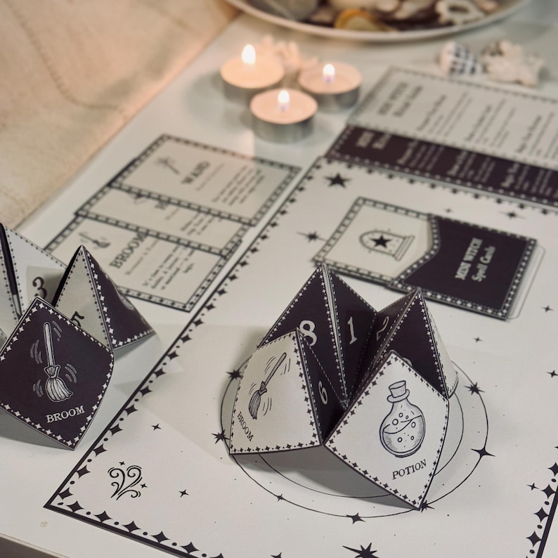 May include: A black and white witch spell card game with a fortune teller style paper fortune. The fortune teller is folded into a pyramid shape with the words "Broom", "Potion", and "Wand" visible. The card game has a black background with white stars and the words "Witch Spell Cards".