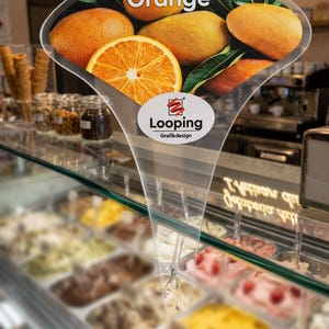 Könnte beinhalten: Ein durchsichtiges Schild für Orangeneis. Das Schild zeigt ein Foto von Orangen und das Wort "Orange" in Weiß. Das Schild hat auch das Logo "Looping Grafikdesign". Es befindet sich vor einer Eisvitrine.