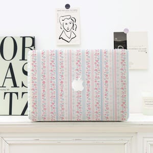 May include: A laptop case with a floral pattern, featuring pink flowers and blue stripes on a white background. The case has a white Apple logo. The case is on a white surface.