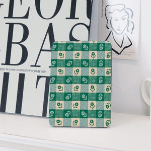 Może przedstawiać: Zielona i biała kratka z małymi białymi kwiatami na tkaninowej podkładce. Podkładka jest prostokątna i ma lekko fakturowaną powierzchnię.