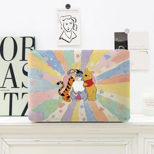 May include: A rectangular case featuring a colorful design with Winnie the Pooh, Tigger, and Eeyore. The background has pastel rays and hearts. The case is on a white shelf with decorative items in the background.