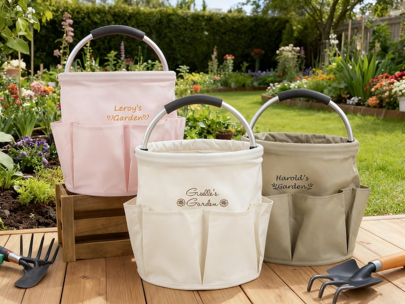 K&ouml;nnte beinhalten: Drei Gartenwerkzeug-Organizer aus Canvas in Rosa, Creme und Beige, jeweils mit Metallgriff und mehreren Au&szlig;entaschen. Auf der rosa Tasche steht "Leroy's Garden". Auf der cremefarbenen Tasche steht "Giselle's Garden". Auf der beigefarbenen Tasche steht "Harold's Garden".