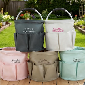 K&ouml;nnte beinhalten: Eine Auswahl an personalisierten Gartentaschen in verschiedenen Farben: Grau, Wei&szlig;, Rosa, Beige und Mintgr&uuml;n. Jede Tasche hat mehrere Au&szlig;entaschen und einen Metallgriff. Die Taschen sind mit Namen und dem Wort "Garden" bestickt.