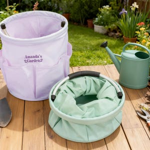 K&ouml;nnte beinhalten: Ein helllila Garten-Eimer mit Taschen und dem Text "Amanda's Garden" neben einem gr&uuml;nen, zusammenklappbaren Garten-Eimer, einer gr&uuml;nen Gie&szlig;kanne, einer kleinen Schaufel und einer Gartenschere auf einer Holzoberfl&auml;che.