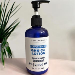 Puede incluir: Una botella de loción azul con un dispensador de bomba negro. La etiqueta dice "XENORGANIX COPPER PEPTIDE GHK-Cu LOTION" y "Normal to Dry Skin Unscented 2% | 2,000 MG 237ML". La botella está frente a una planta verde.