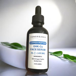 Puede incluir: Una botella de vidrio marrón oscuro de XENORGANIX Copper Peptide GHK-Cu Face Serum. La etiqueta incluye el texto "4% | 2.400 MG" y "2 OZ (60ML)". La botella tiene una tapa cuentagotas negra. Hojas verdes y un cuenco blanco en el fondo.