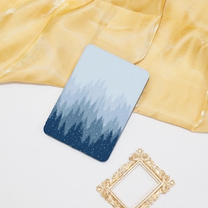 Op de afbeelding: Een rechthoekige onderzetter met een winterbosontwerp in tinten blauw en wit. De onderzetter heeft een donkerblauw bos aan de onderkant, dat overgaat in lichtere blauwe bomen en een besneeuwde lucht. Een goudkleurig decoratief frame bevindt zich in de rechter benedenhoek.