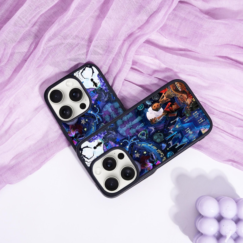 May include: Two black phone cases with a colorful, fantasy-themed design. The cases feature a dark blue and purple background with illustrations of a person, buildings, and other elements. The cases have a black border and a white camera module.