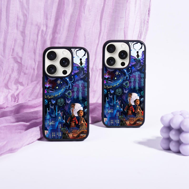 May include: Two black phone cases with a colorful illustration featuring a fantasy scene with characters, a blue house, and the text "Be Careful What". The cases have a glossy finish and are set against a purple fabric background.