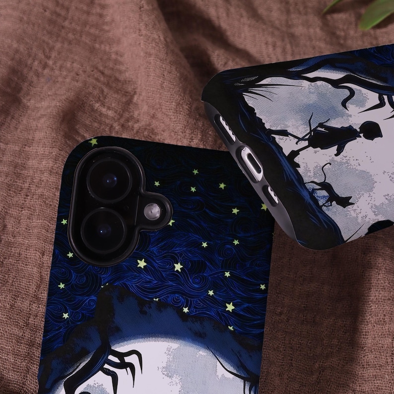 May include: Two phone cases with a dark blue night sky design, featuring a full moon, stars, and a silhouette of a figure. One case shows the camera lenses. The other case has a silhouette of a figure in a tree.