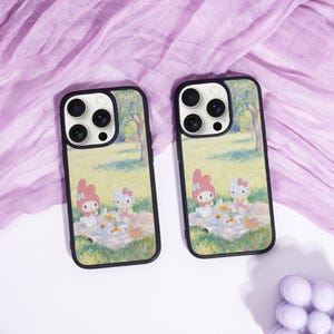 Puede incluir: Dos fundas para tel&eacute;fono con bordes negros. Cada funda presenta una escena de picnic con personajes de dibujos animados, ambientada en un parque con &aacute;rboles. Las fundas est&aacute;n sobre una superficie blanca con una tela morada.