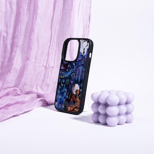 May include: Black phone case with a colorful illustration featuring a fantasy scene with characters and a castle. A lavender bubble candle sits next to the phone case. A lavender fabric is in the background.
