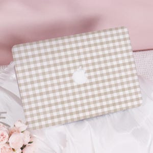 Peut inclure: Une peau d'ordinateur portable beige avec un motif vichy blanc. Le logo Apple est visible sur la peau.