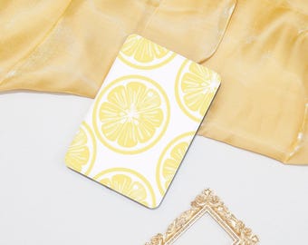 May include: White laptop case with a lemon pattern. The lemons are yellow and have a white background. The case is on a yellow fabric background.