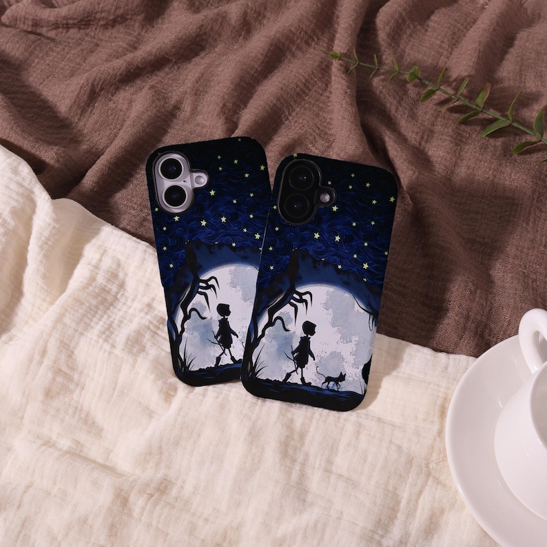 May include: Two black phone cases with a nighttime scene featuring a full moon, silhouettes of figures, and a starry sky. The cases have a dark blue and black color scheme, with a whimsical, fantasy theme.