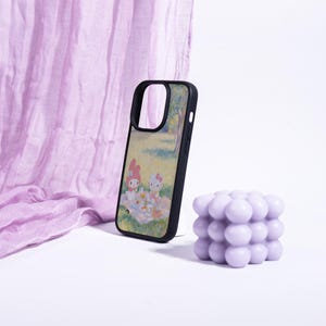 Puede incluir: Funda de tel&eacute;fono negra con una colorida ilustraci&oacute;n de dos personajes de dibujos animados haciendo un picnic en un parque. Una vela de burbujas lavanda y una tela lavanda est&aacute;n en el fondo. La funda del tel&eacute;fono es un accesorio de protecci&oacute;n.
