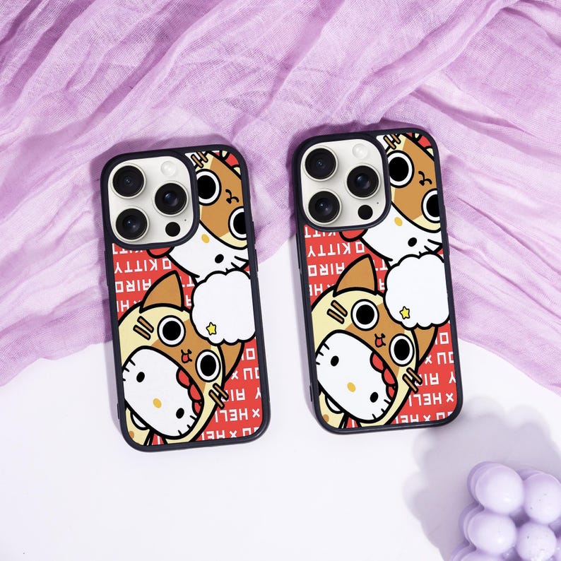 May include: Two black phone cases with a cartoon design featuring a cat character in a costume. The cases have a red background with white text. The cat is brown, white, and yellow.
